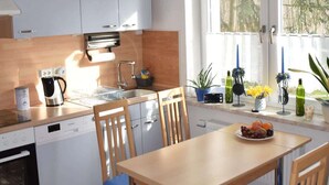A modern kitchen with white cabinets, a wooden dining table with blue chairs, and a window with blue curtains. - Maaß'ens vacation home (Wildau)