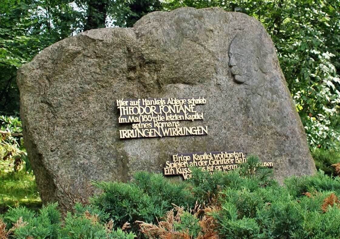 A large stone monument with inscriptions in a foreign language, surrounded by greenery.