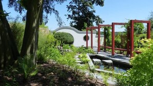 A garden with a pond, red wooden structures, and a white curved wall. - Maaß'ens vacation home (Wildau)