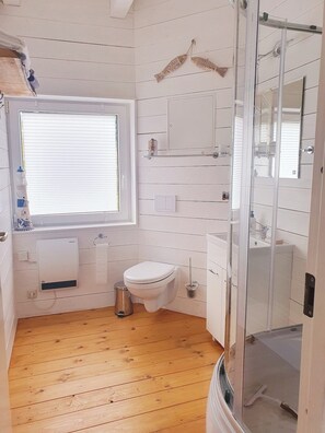A compact bathroom with a toilet, sink, and a glass-enclosed shower area. - Haus Svensson Altheide A (Ribnitz-Damgarten)