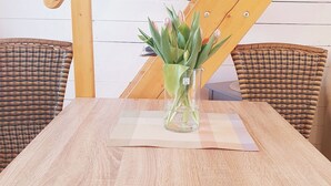 A dining table with a glass vase of flowers, surrounded by wicker chairs.