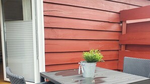 A patio with a table and four chairs, a potted plant, and a red exterior wall.
