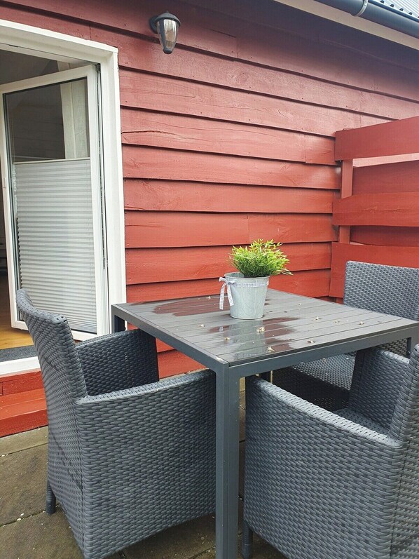 Een terras met een tafel en vier stoelen, een bloempot en een rode buitenmuur.