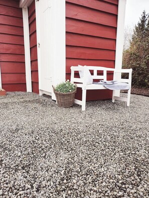 A white bench with a basket of flowers in front of a red building.