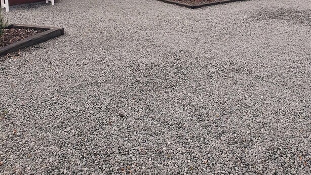 A red building with a metal roof, a white bench, and a gravel driveway.