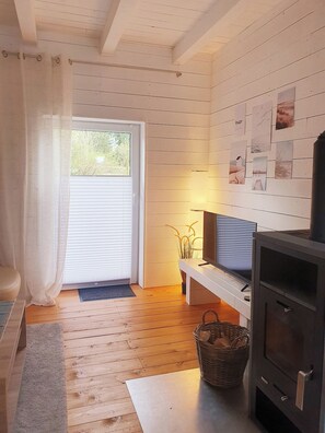 A cozy room with a wooden floor, a television on a stand, a fireplace, and a door leading outside.