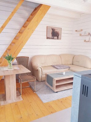 A cozy living room with a sofa, a coffee table, a wicker chair, and a wooden staircase.