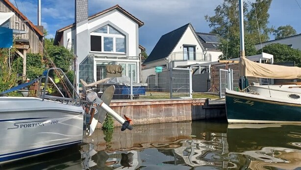A marina with boats docked, a house with a large window, and a metal fence in the background.