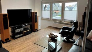 A modern living room with a large flat-screen TV, a comfortable black sofa, and a glass coffee table.