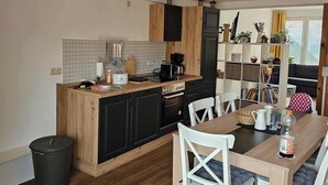A compact kitchen with wooden cabinets, a central island, and a dining area with white chairs.