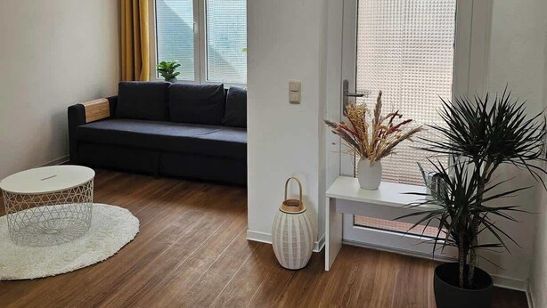 A modern living room with a dark sofa, a round coffee table, and a potted plant.