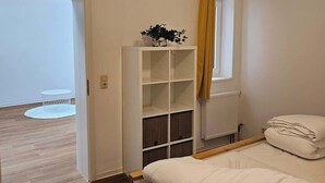 A bedroom with a bed, a white wardrobe, a window with curtains, and a view of a balcony.