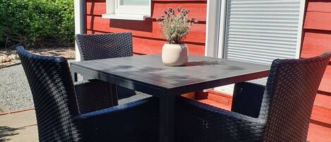 An outdoor patio with a table and chairs, a potted plant, and a red building with windows.