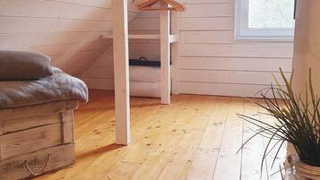 Una habitación con suelo de madera, una cama en altillo, un ventanal y una planta.