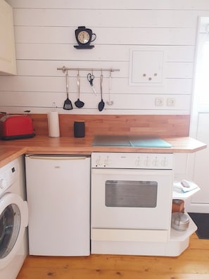 A compact kitchen with a washing machine, a small oven, a toaster, and a clock on the wall.