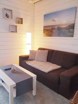 Una sala de estar con un sofá marrón, una mesa de centro blanca y un cuadro en la pared.