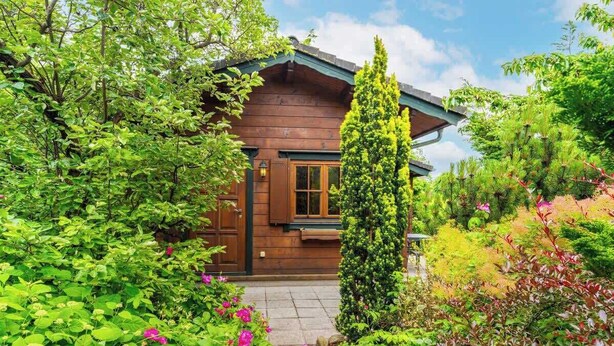 A wooden cabin surrounded by lush greenery and flowering plants. - House Svenja (Koserow)