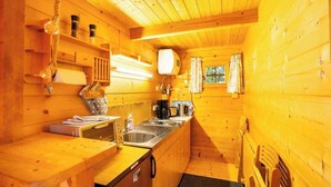 A compact wooden cabin with a kitchenette, a hanging light fixture, and a window with curtains. - House Svenja (Koserow)