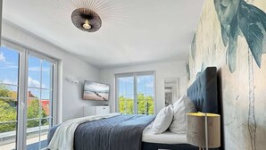 Ein Schlafzimmer mit einem Bett, einem Fernseher, einer Lampe und einem großen Fenster.