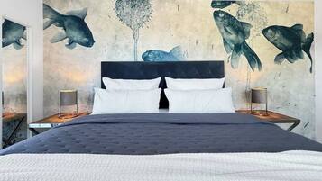 Ein Bett mit dunklem Kopfteil, weißen Kissen und einer gesteppten Decke. Zwei Nachttische mit Lampen und ein großes Wandbild von Fischen sind ebenfalls zu sehen.