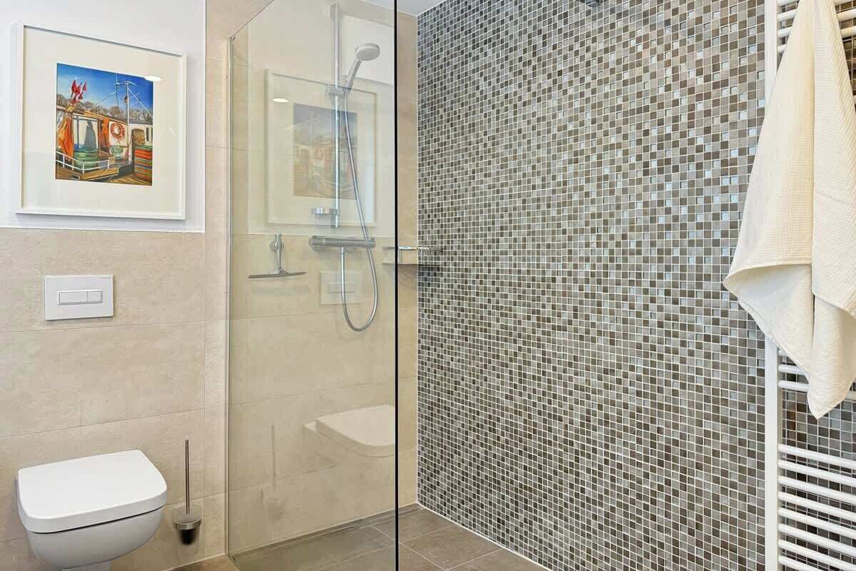 Un bagno moderno con cabina doccia in vetro, un water bianco e una parete rivestita in mosaico.