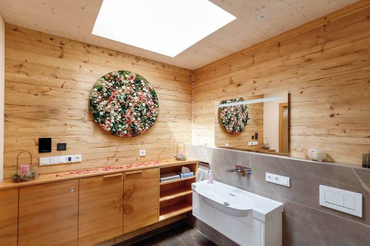Ein modernes Badezimmer mit Holzwänden, einem Dachfenster, einer runden Wanddekoration mit floralem Muster, einem Waschtisch mit Spiegel und einer Badewanne.