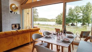 A dining area with a wooden table set for four, a sofa, and a view of a lake. - Refugio del Lago Zechlin (Rheinsberg)
