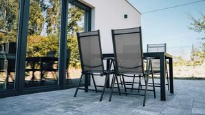 Un patio moderno al aire libre con una mesa, sillas, ventanas amplias y vistas a árboles.