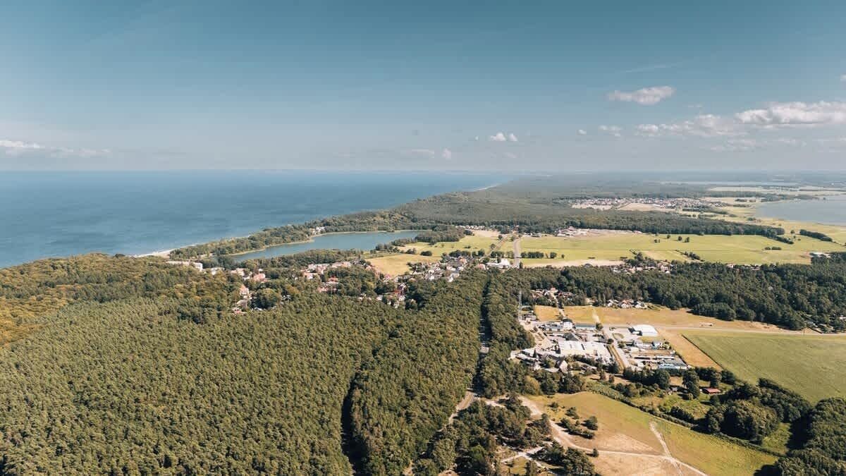 Vista aérea de uma área costeira com uma cidadezinha, florestas densas e uma grande extensão de água.