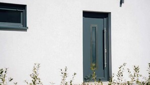 Fachada moderna de un edificio con puerta y ventana, rodeada de vegetación.