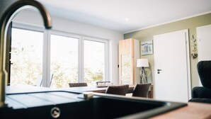 Cocina moderna con pileta, zona de comedor con mesa y sillas, y vista al exterior a través de amplios ventanales.