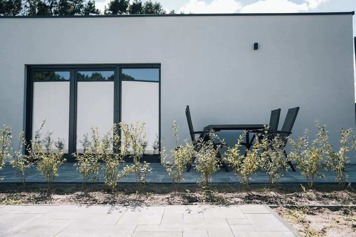 A modern building with a large glass door and a small outdoor seating area with a table and chairs.