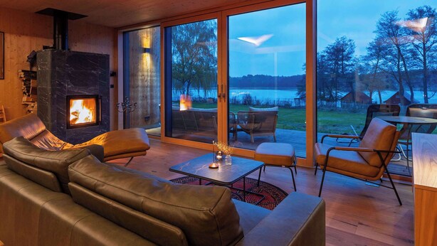 Una sala de estar moderna con chimenea, sofá de cuero y grandes puertas corredizas de vidrio que dan a una terraza al aire libre.