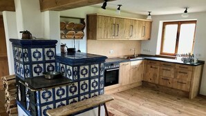 Een keuken met een blauw-witte betegelde kachel, houten kasten en een houten bankje.