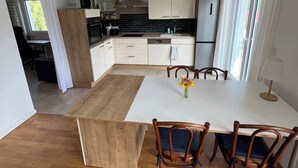A modern kitchen with white cabinets, a black backsplash, and a wooden dining table with four chairs. - Buschwiesen Ausguck (Teltow)