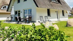 Una casa con techo de paja, ventanas grandes y un patio con mobiliario exterior.