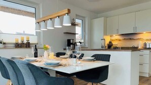 Una cocina moderna con armarios blancos, una isla central y una zona de comedor con sillas azules y una mesa blanca.