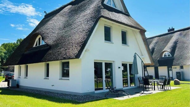 Una casa blanca con techo de paja negra, un patio con muebles de exterior y un cielo azul claro.