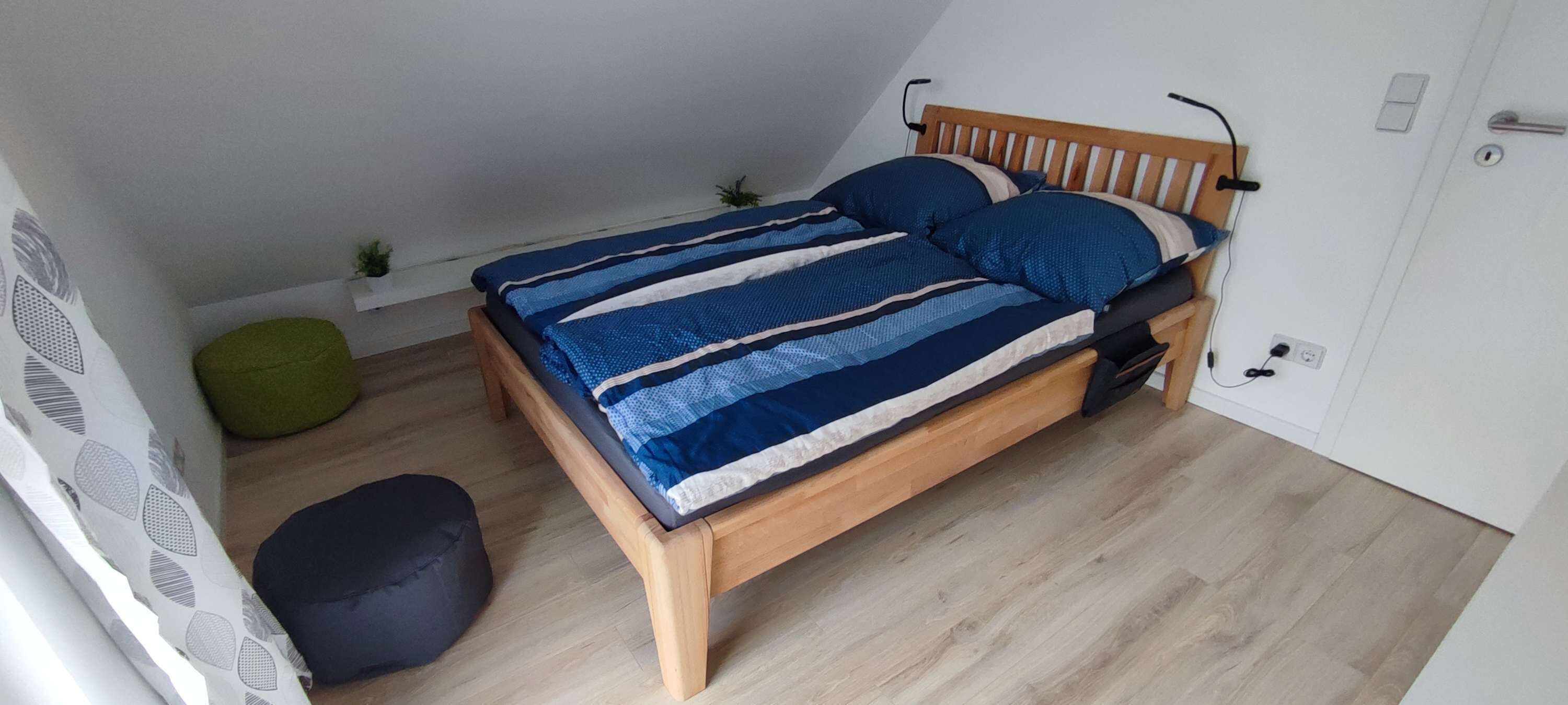 Ein Schlafzimmer mit einem hölzernen Bett, einem grünen Sitzsack, einem schwarzen Hocker und einer kleinen Pflanze.