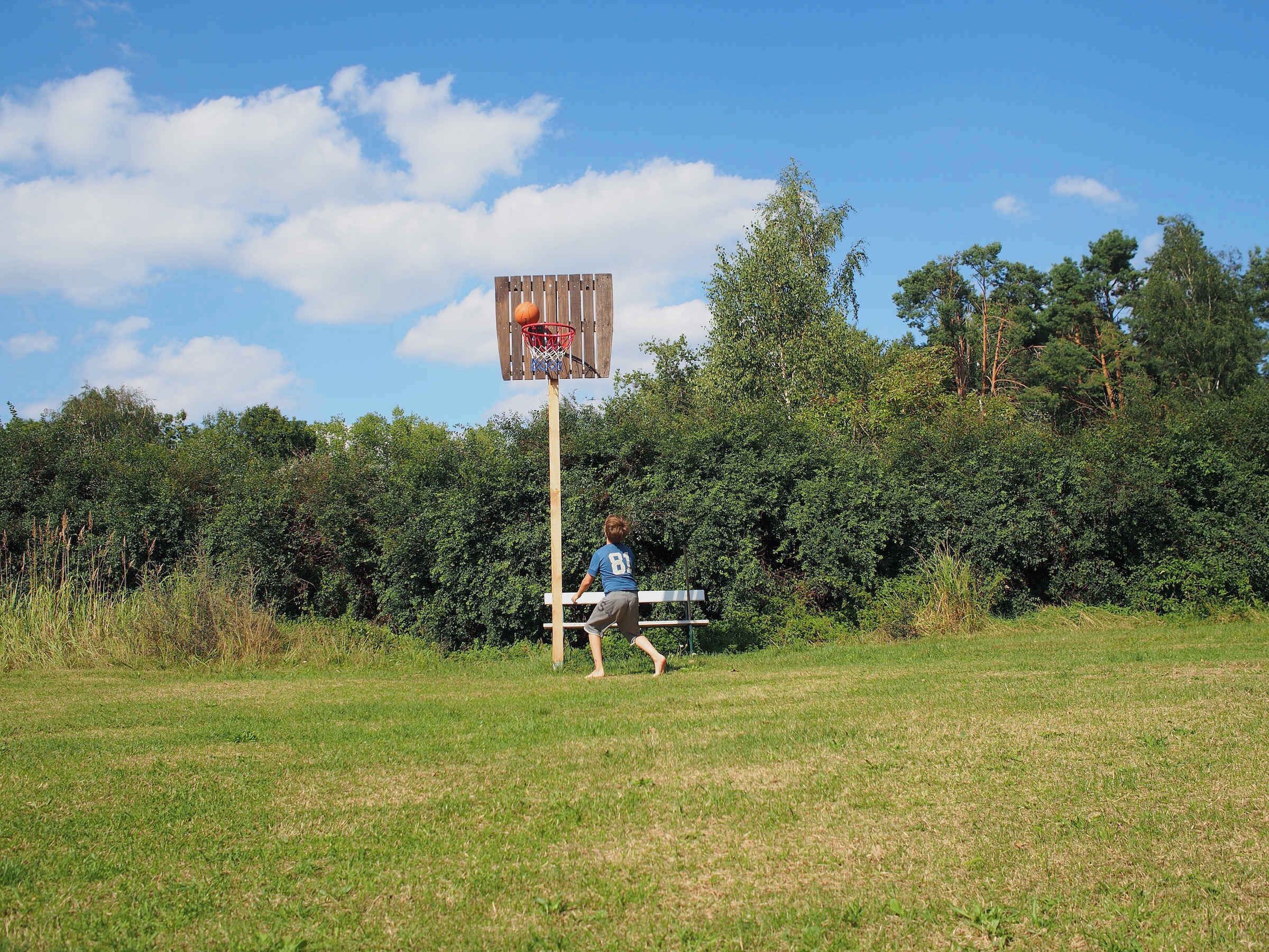 A basketball hoop in an open field with a wooden bench nearby.