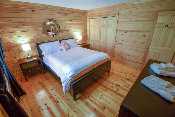 Un dormitorio con paneles de madera, una cama, lámparas de noche, un espejo y un armario de madera.