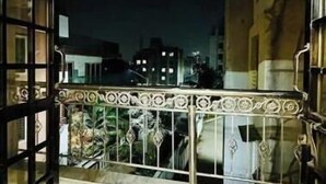 Een open balkon met een metalen hekwerk, uitzicht op gebouwen in de verte, en een marmeren vloer.