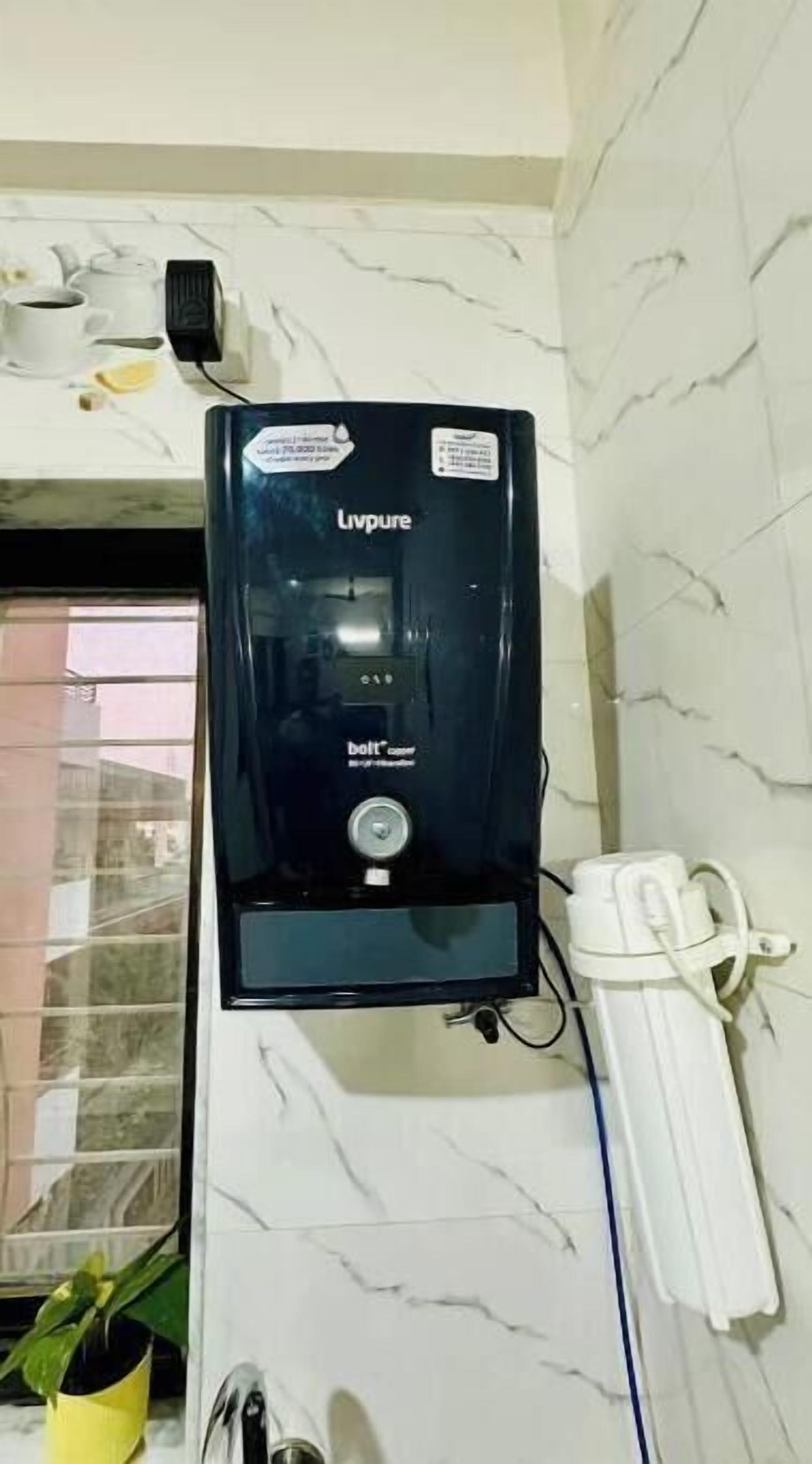 A black Livpure water dispenser mounted on a wall with a marble pattern.