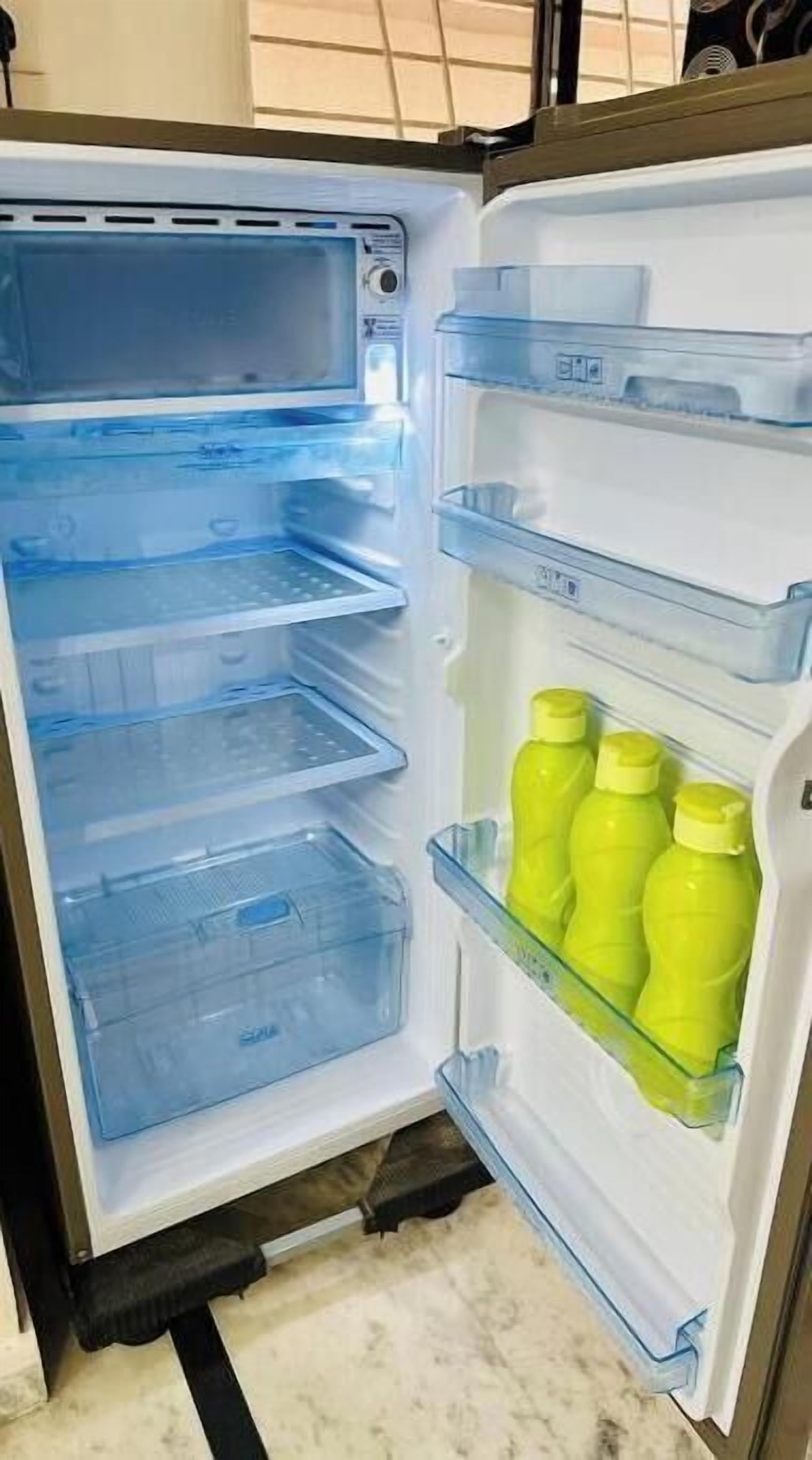 Un réfrigérateur ouvert, doté d’étagères en plastique transparent et d’un distributeur d’eau.