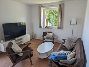 En stue med et fladskærms-tv, to lædersofaer, et lille rundt bord og et vindue med gardiner.