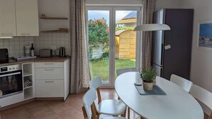 Een kleine keuken met een eethoek, een inbouwoven, een koffiezetapparaat en uitzicht op een tuin door een glazen deur.