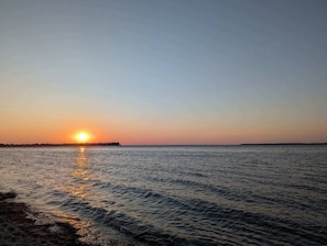 Un atardecer sobre una superficie de agua tranquila con una costa lejana.