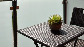 A balcony with a metal table and a potted plant, overlooking a residential area with houses and trees. - Barther  Hafensonne (Barth)