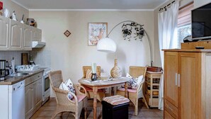 A kitchen with a dining table, wicker chairs, a white pendant lamp, and a TV on a wooden cabinet.
