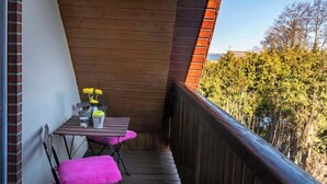 A wooden balcony with a table and chairs, a railing, and a view of trees.